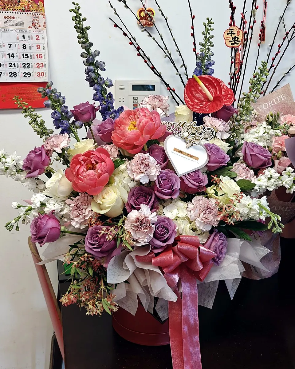 Mother's Day floral arrangement with pink peonies, purple roses, white flowers, and a pink ribbon