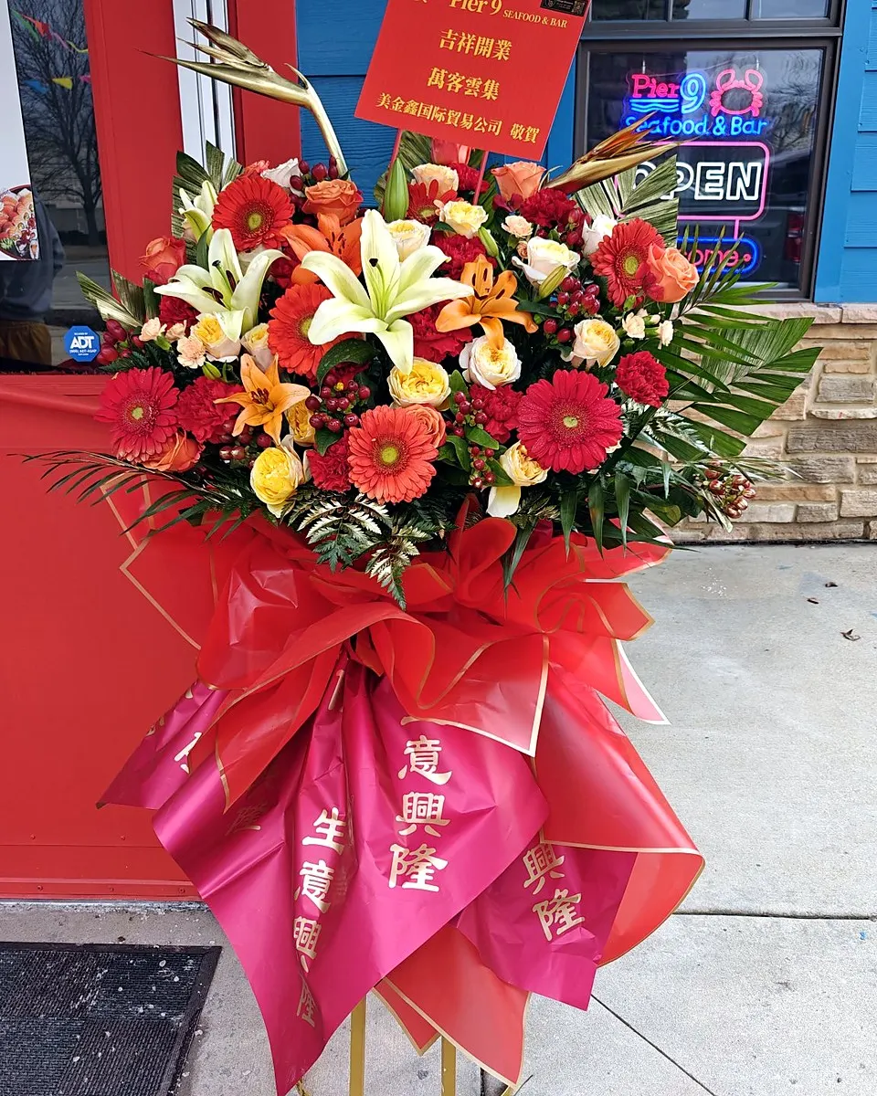 Red and gold grand opening flower stand with red blooms and a ribbon bow