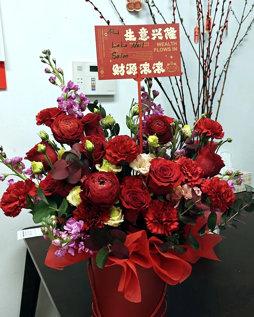 Red roses, carnations, and ranunculus arranged in a red hatbox for a grand opening