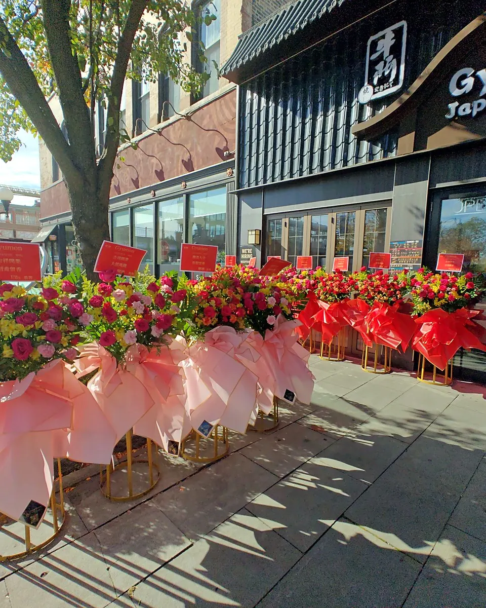A long row of pink and red grand opening flower stands outside a storefront