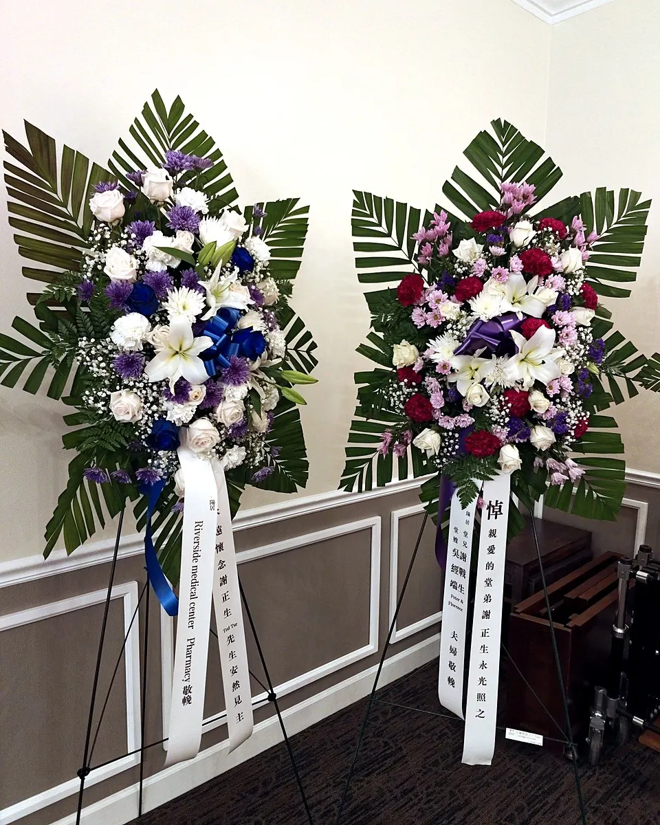 Two purple, white, and burgundy standing funeral sprays with palm leaves