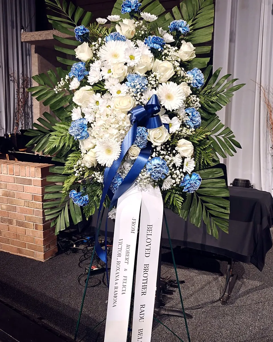 Blue and white standing funeral spray with carnations, roses, daisies, and hydrangeas