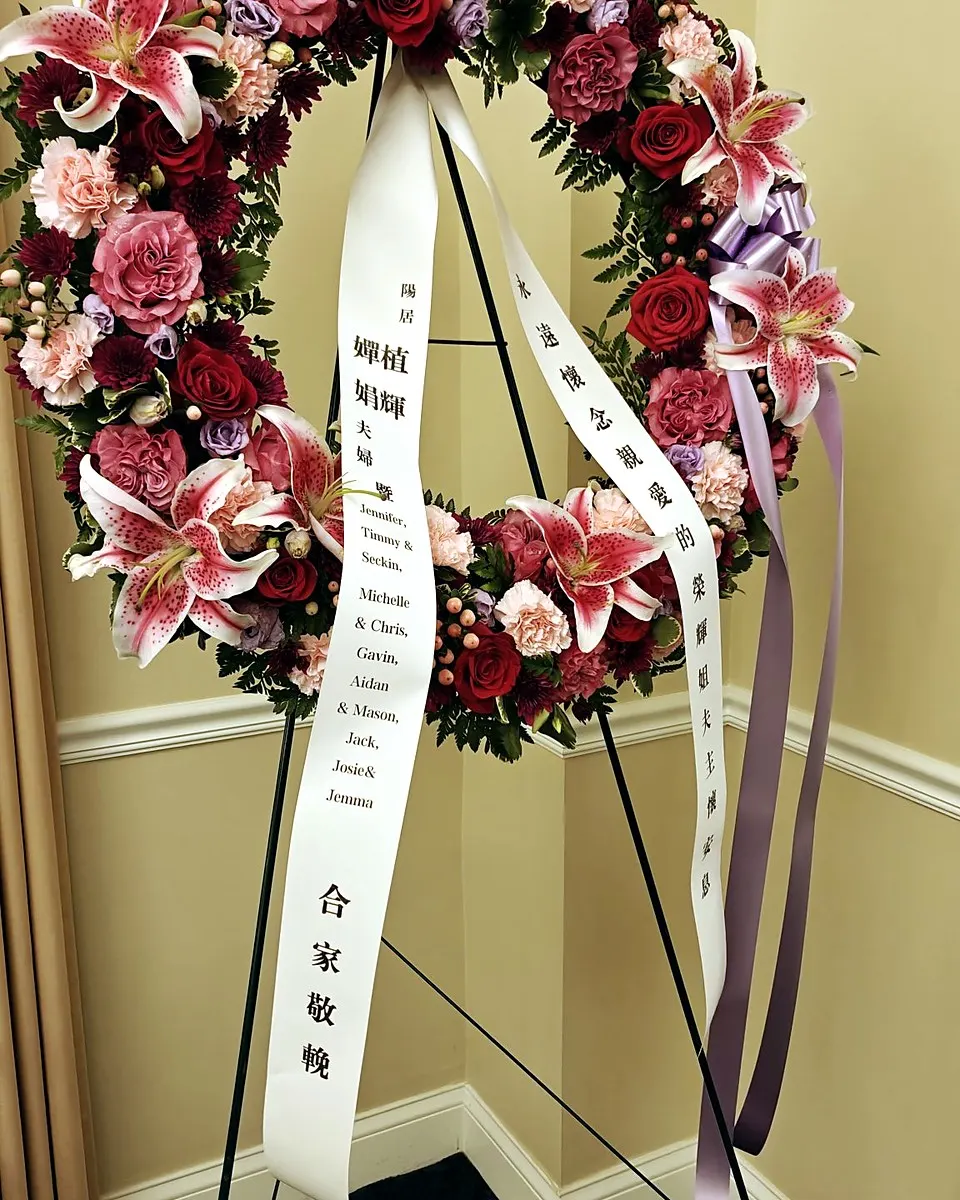 Yellow and white funeral tribute with roses and lilies arranged beneath a memorial medallion