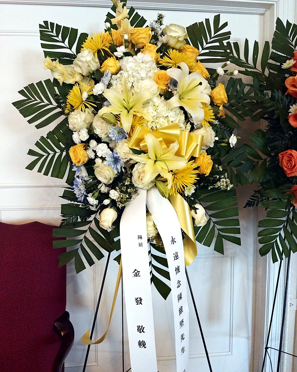 Yellow and white standing funeral spray with lilies, roses, and hydrangeas