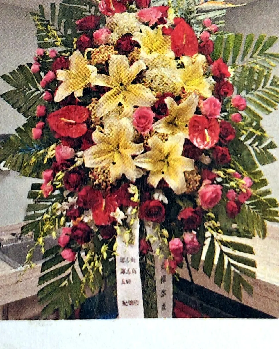 Red and golden-yellow standing funeral spray with lilies and tropical foliage