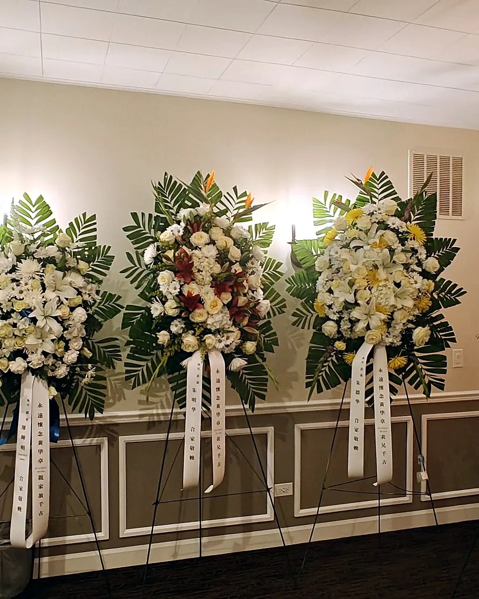 A line of five standing funeral sprays in white, yellow, pink, and red