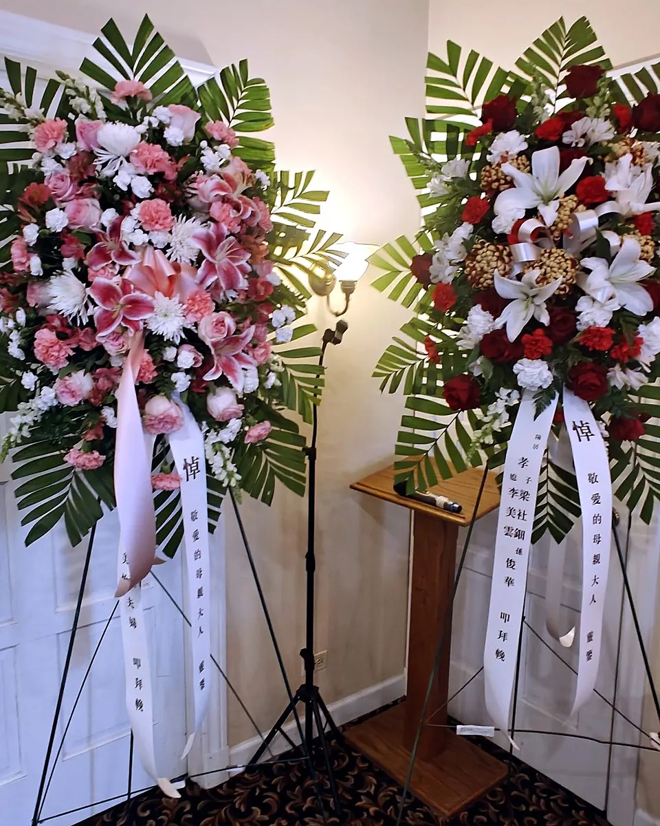 Pink and red standing funeral sprays with lilies, roses, and palm foliage