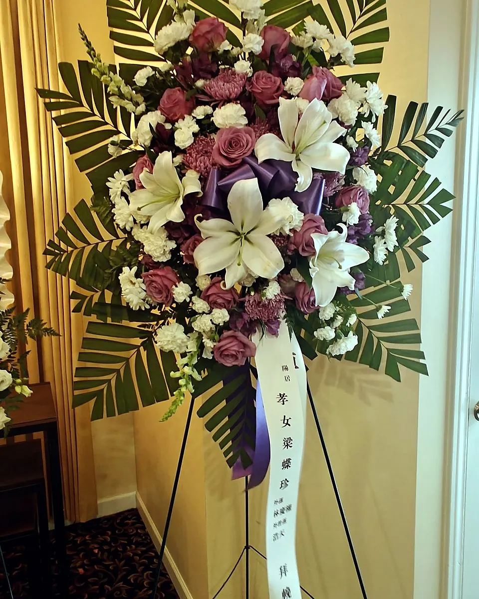 Standing funeral spray with mauve roses, white lilies, and a purple ribbon bow