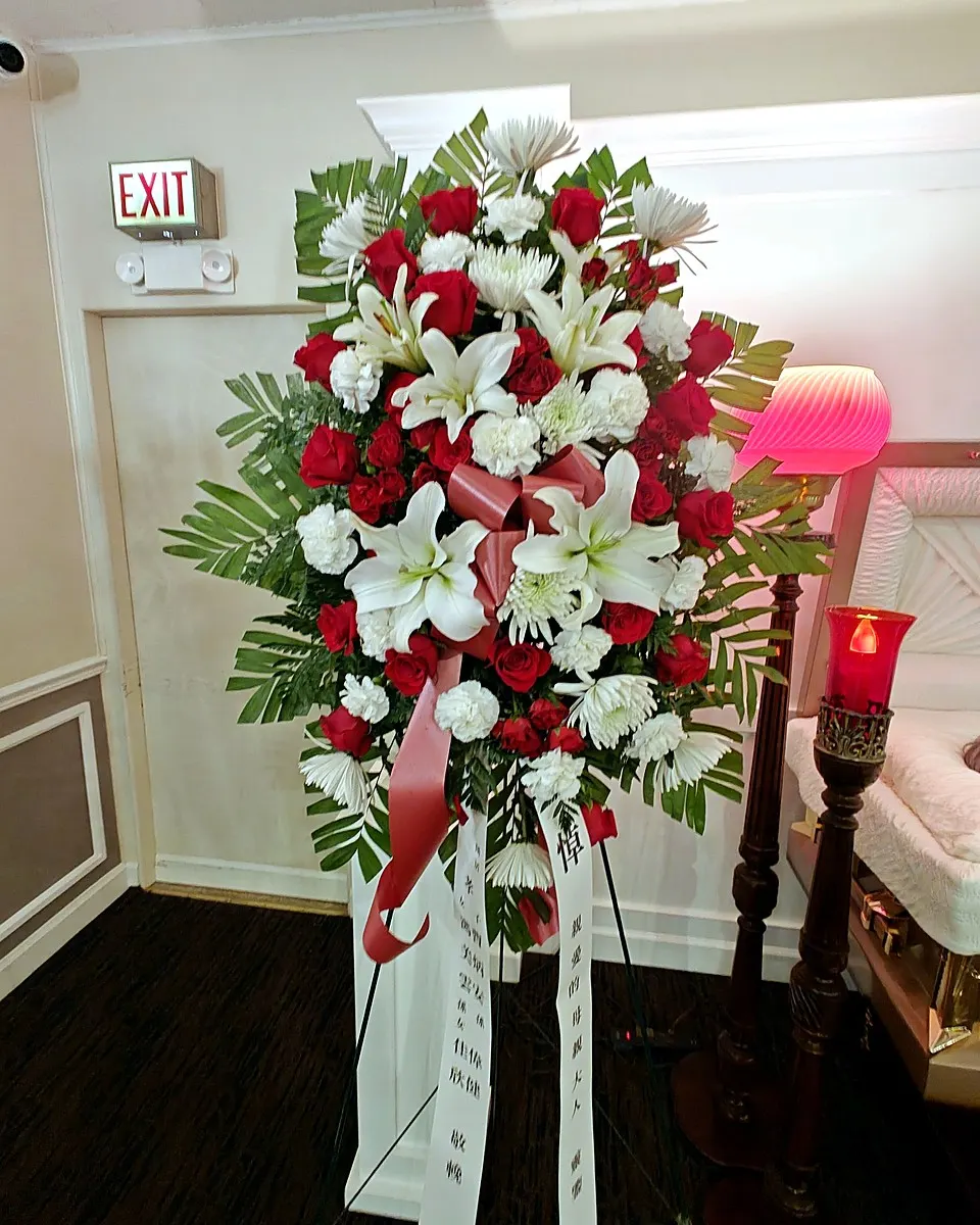 Red and white standing funeral spray with roses, lilies, and chrysanthemums