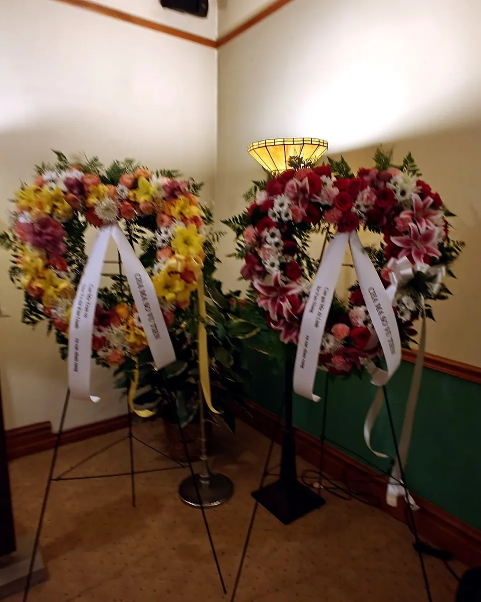 Three standing funeral sprays in yellow, red, white, and blush pink