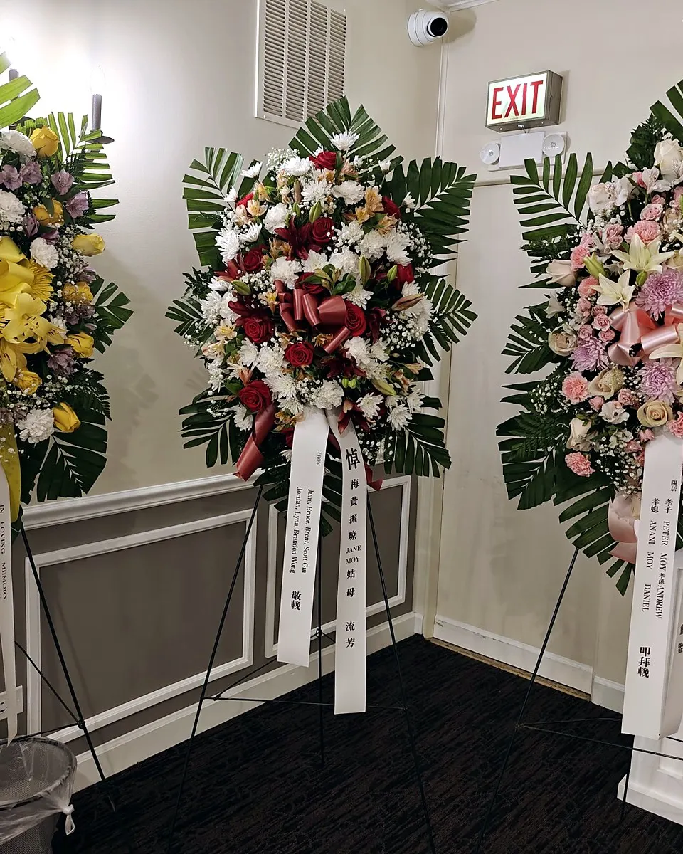 Four standing funeral sprays in burgundy, blue and yellow, white, and pastel pink
