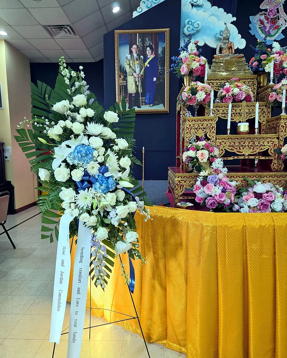 Blue and white standing sympathy arrangement beside ceremonial flowers