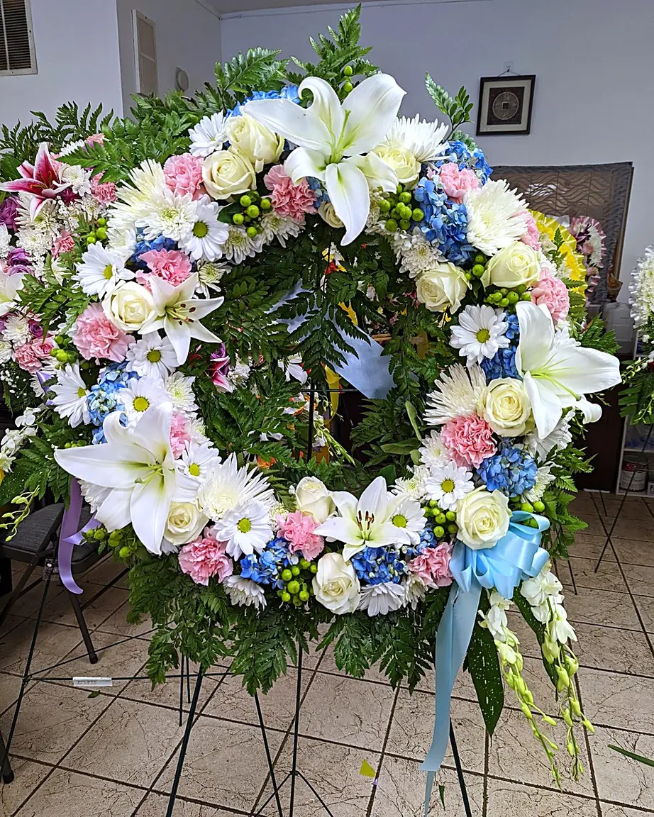 Funeral wreath with white lilies, blue hydrangeas, and pink carnations