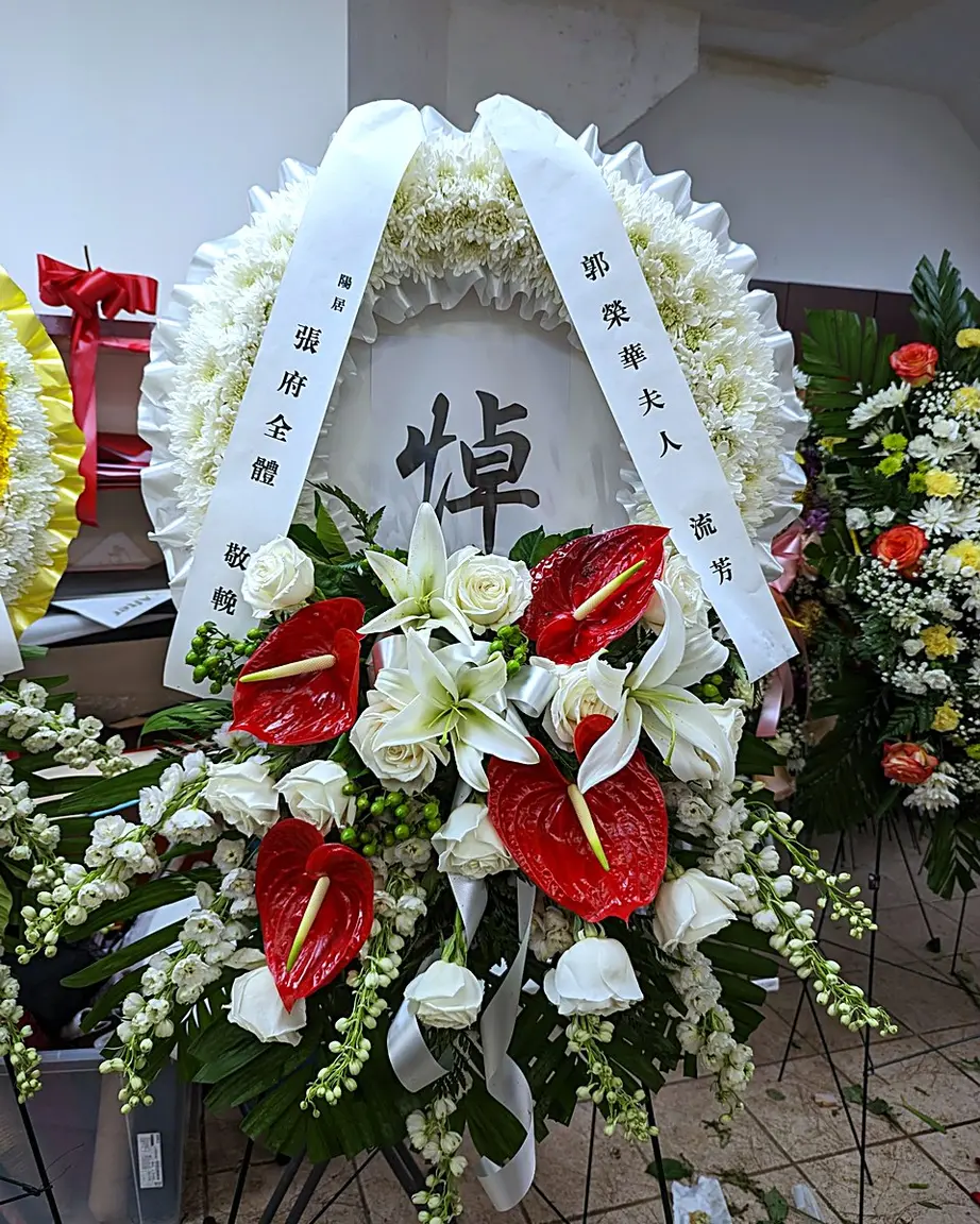 White chrysanthemum funeral wreath with red anthuriums, white roses, and lilies